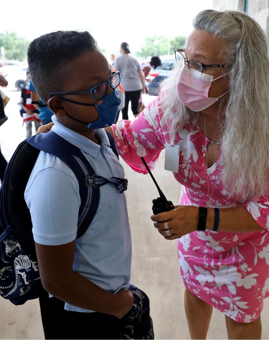 A teacher from Judson ISD is photographed wearing a face mask bending over to speak to a student on campus.